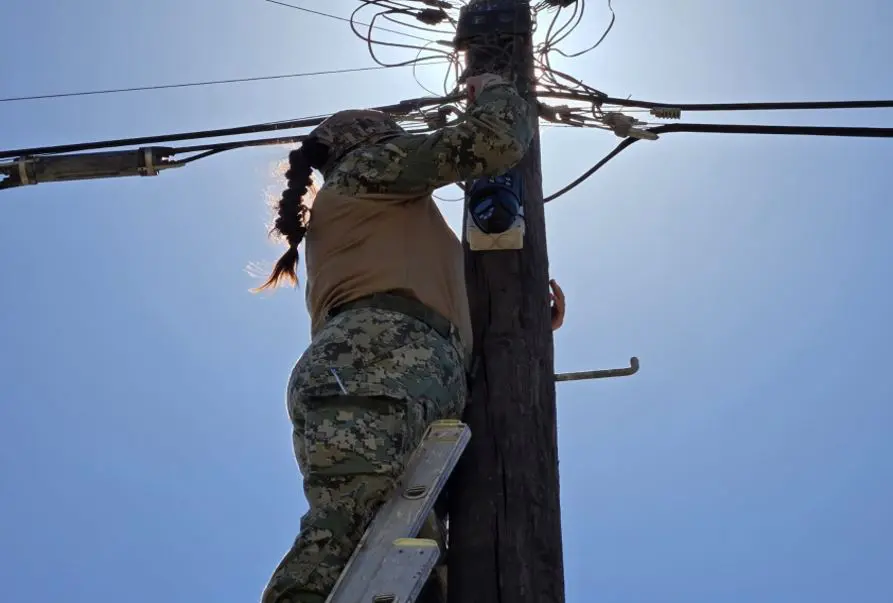 Person on ladder fixing utility pole wires.