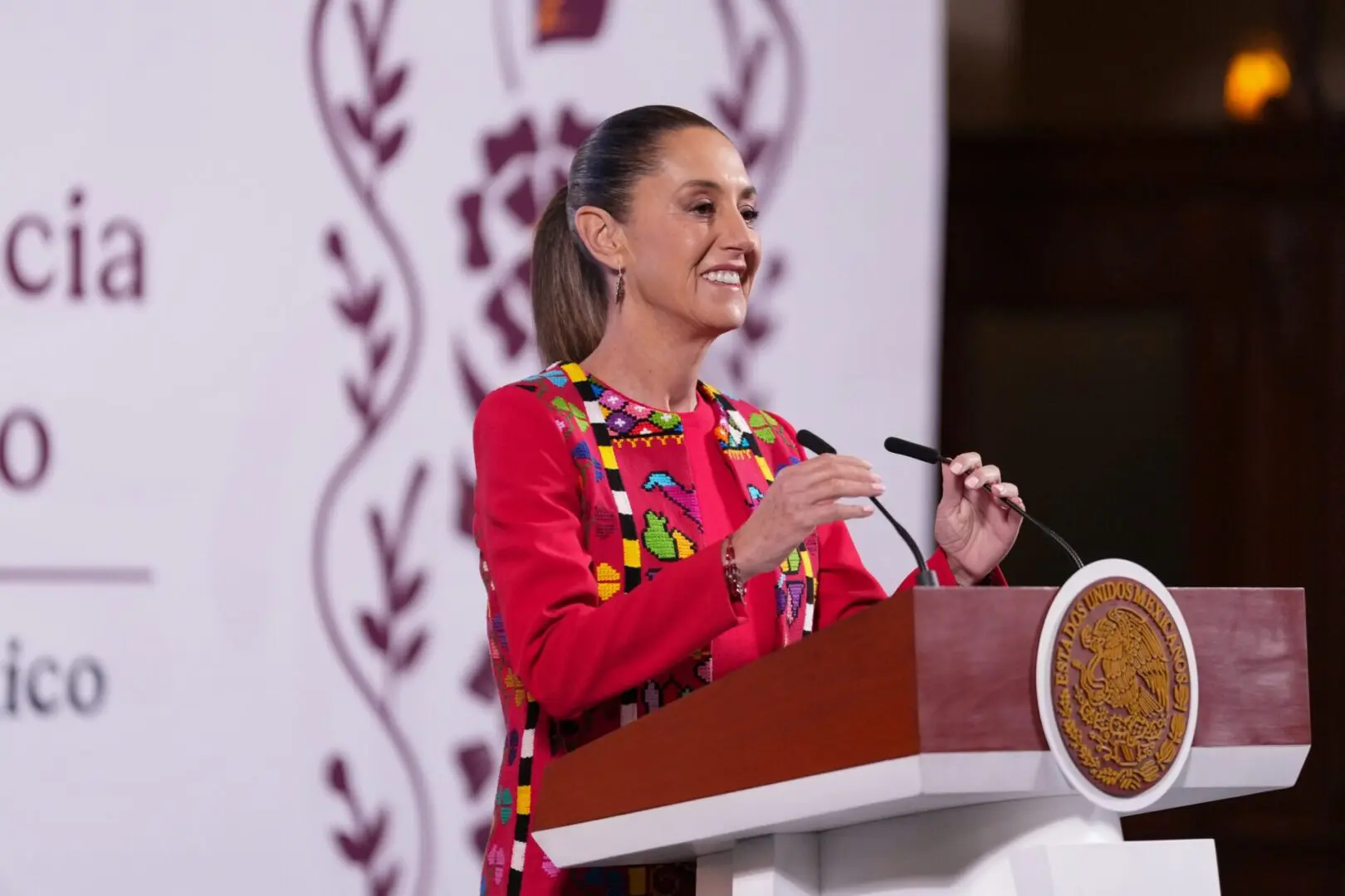 Woman speaking at a podium, smiling confidently.