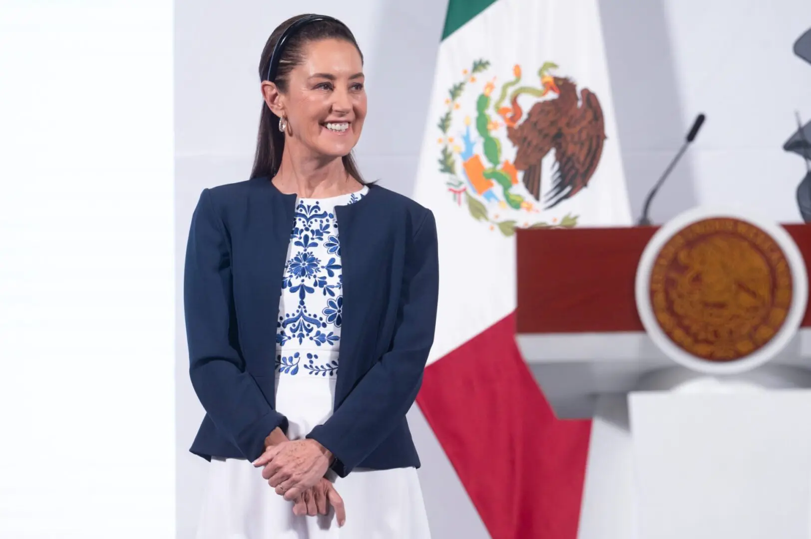 Woman smiling near Mexican flag and podium.
