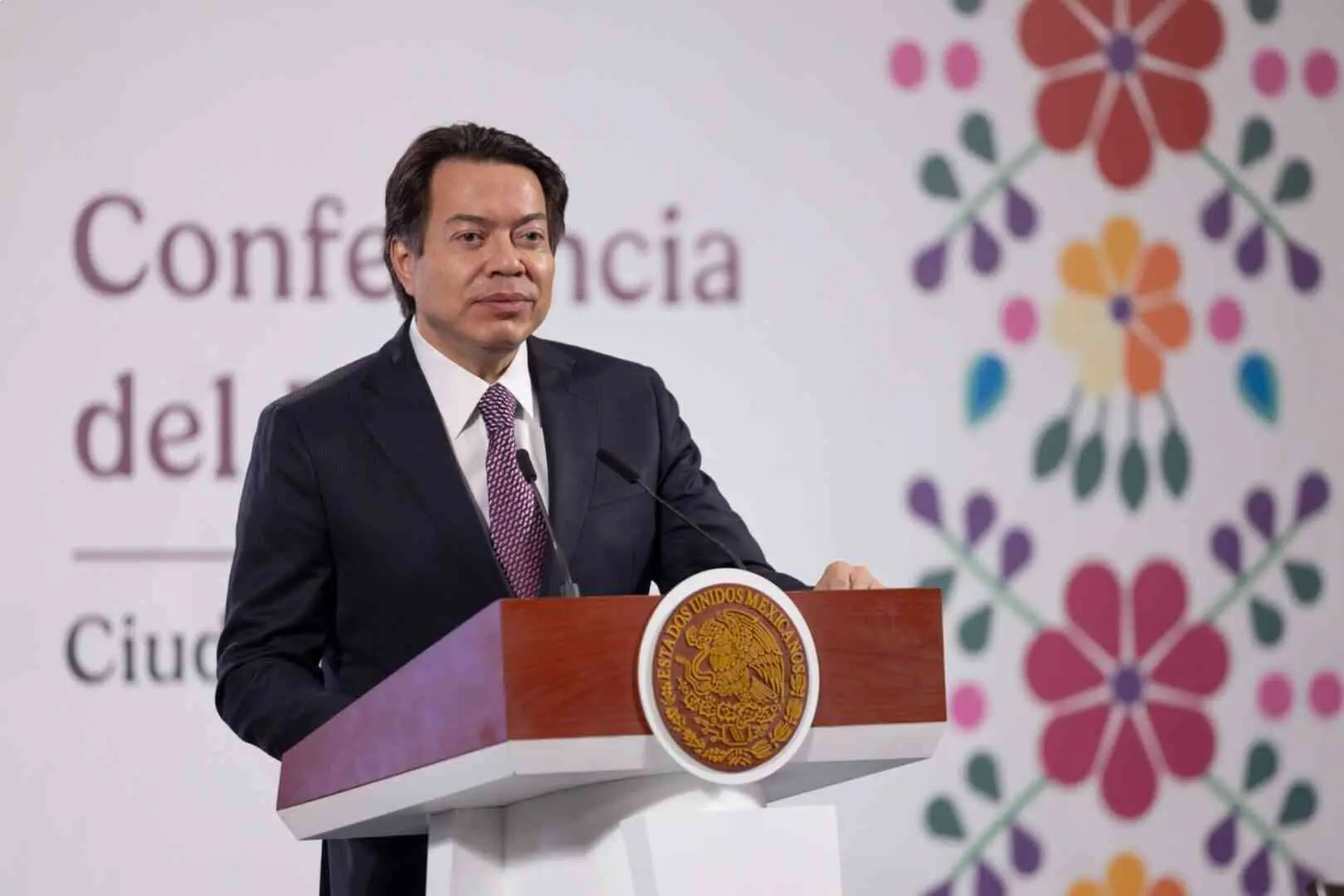Man speaking at podium with floral backdrop.