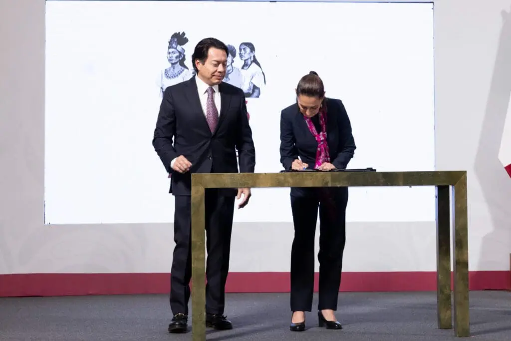 Two people signing documents on a stage, one man and one woman.