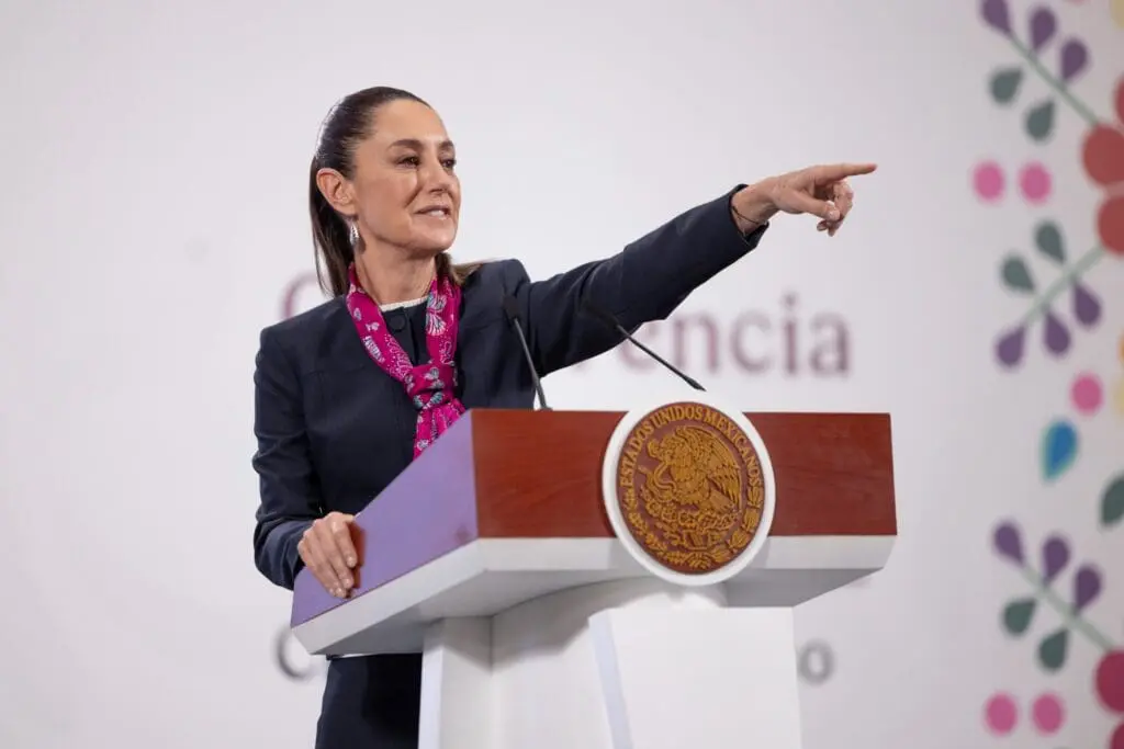 A woman in formal attire pointing while speaking at a podium.