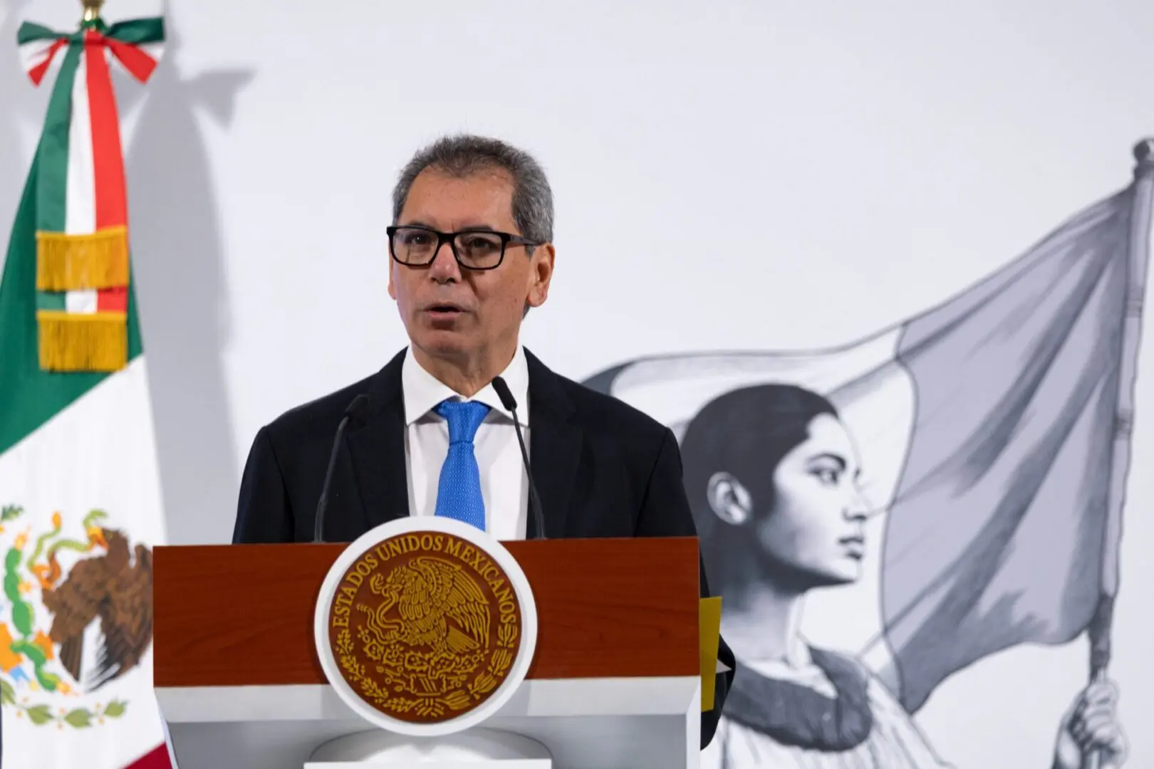 Man speaking at podium with Mexican flag.