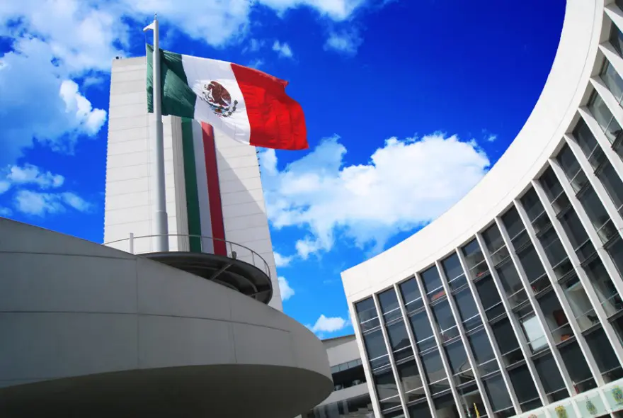 Mexican flag waving on modern building rooftop.