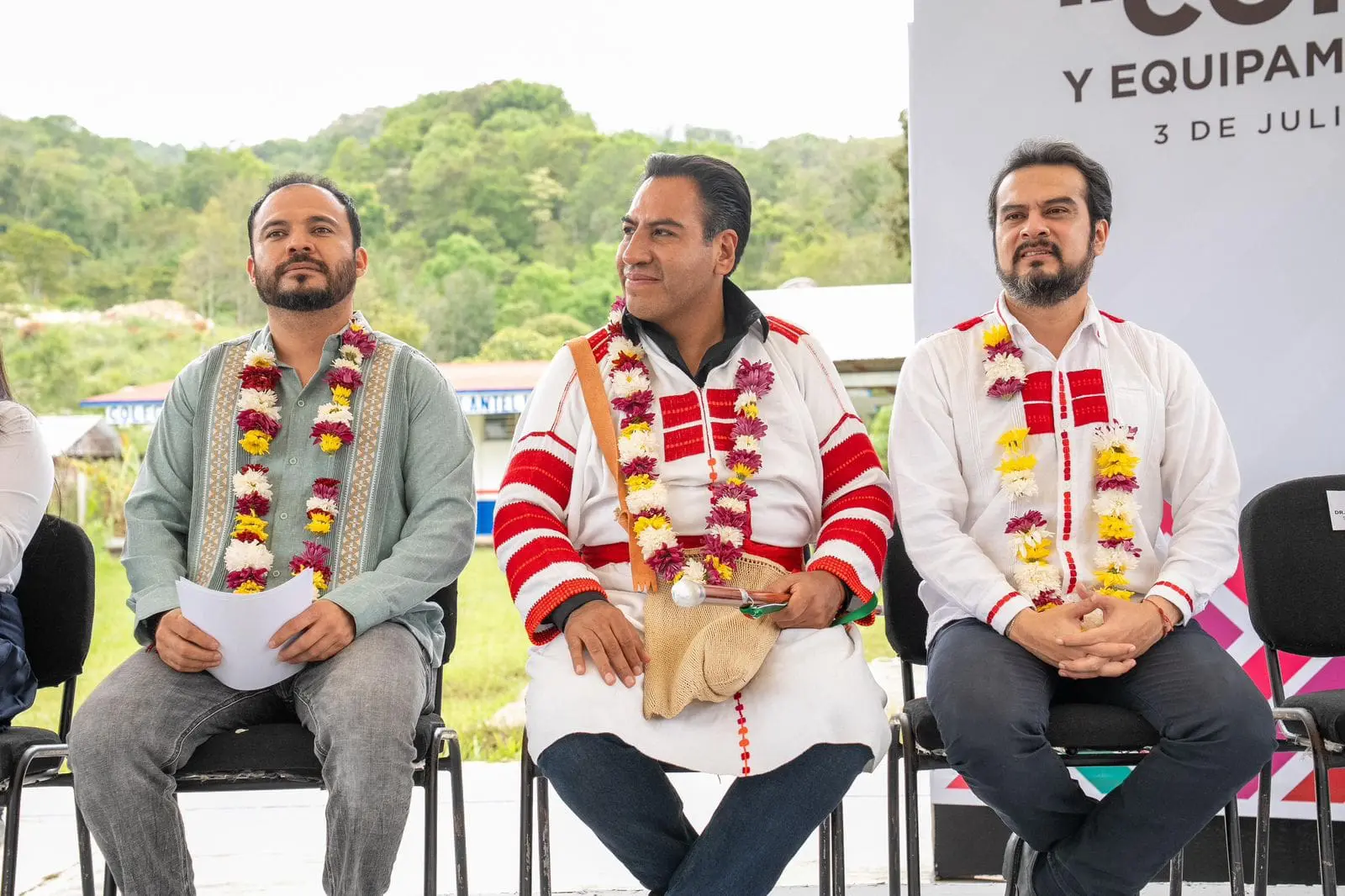 Three men seated wearing colorful flower necklaces.