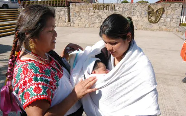 Mujer indígena y madre con recién nacido afuera de hospital en México.