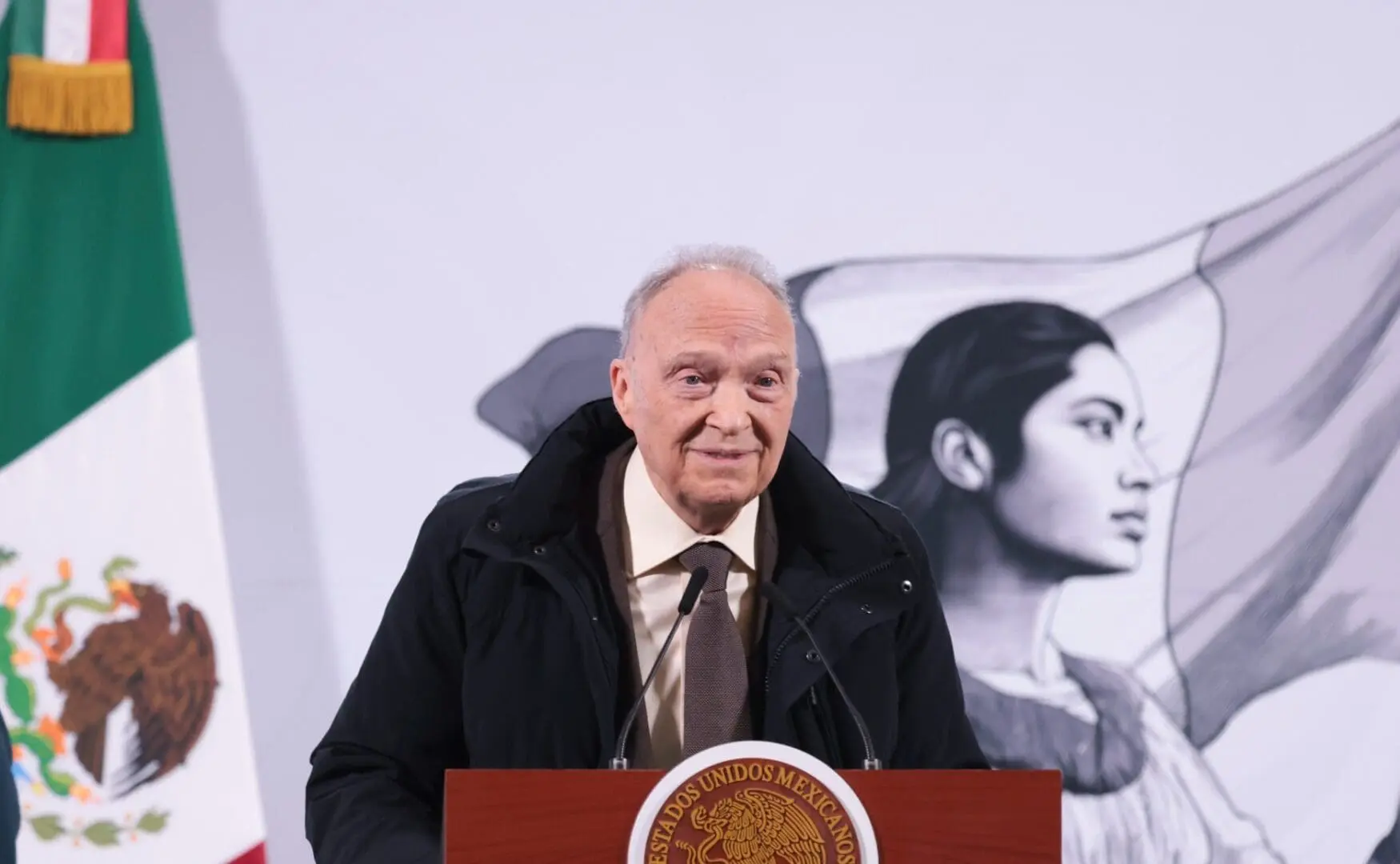 Man delivering speech before Mexican flag mural