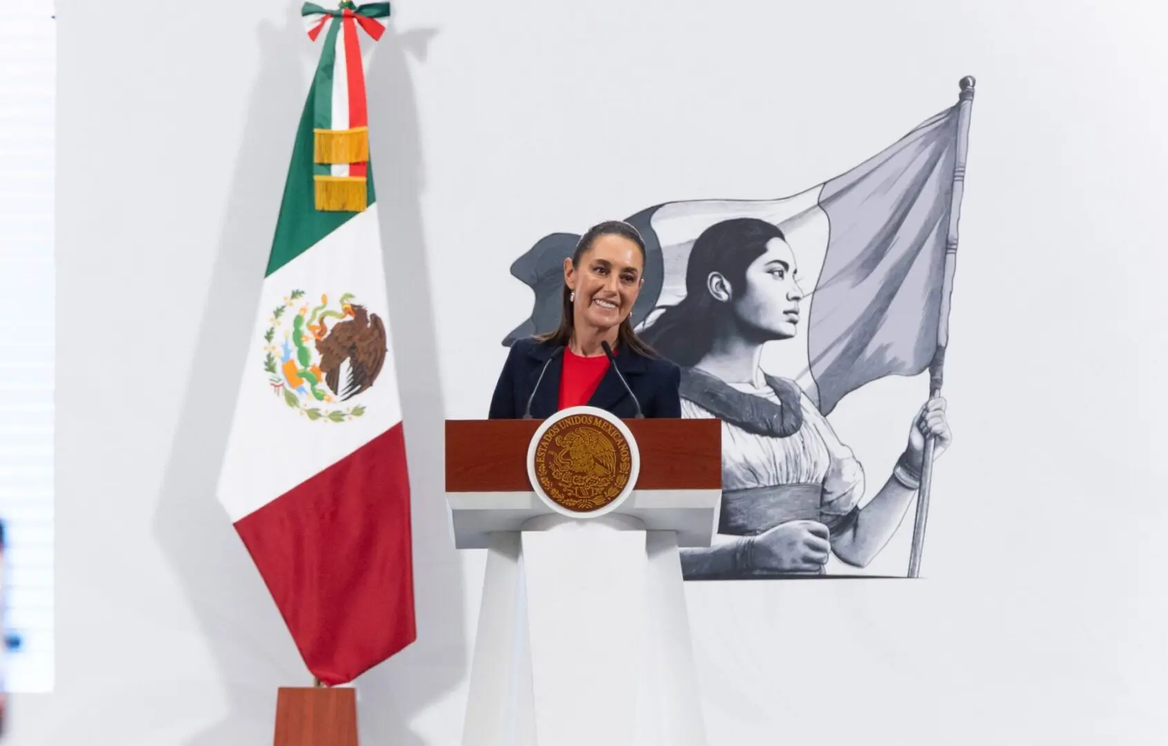 Female speaker at podium with Mexican flag mural