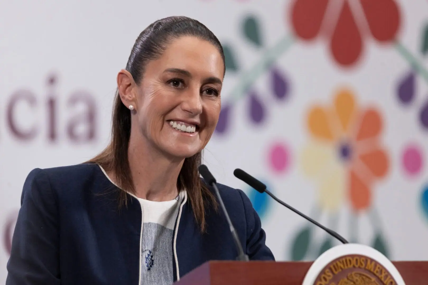 Smiling woman speaking at podium, floral backdrop