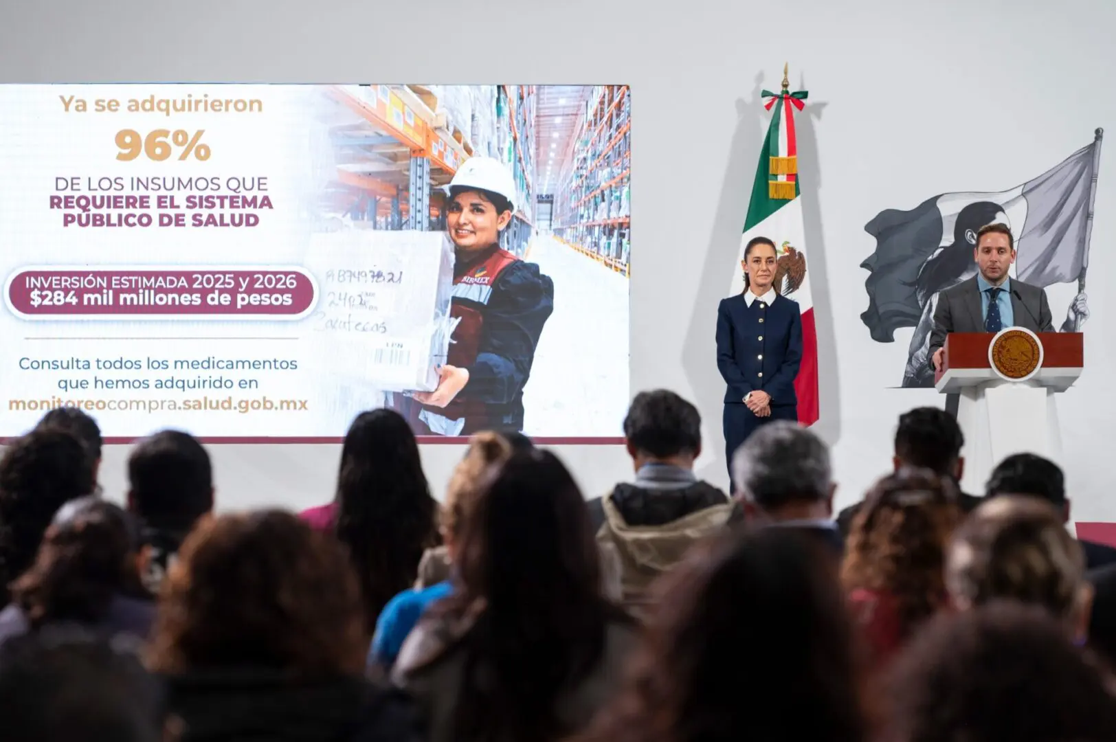 Speaker at podium with Mexican flag, audience