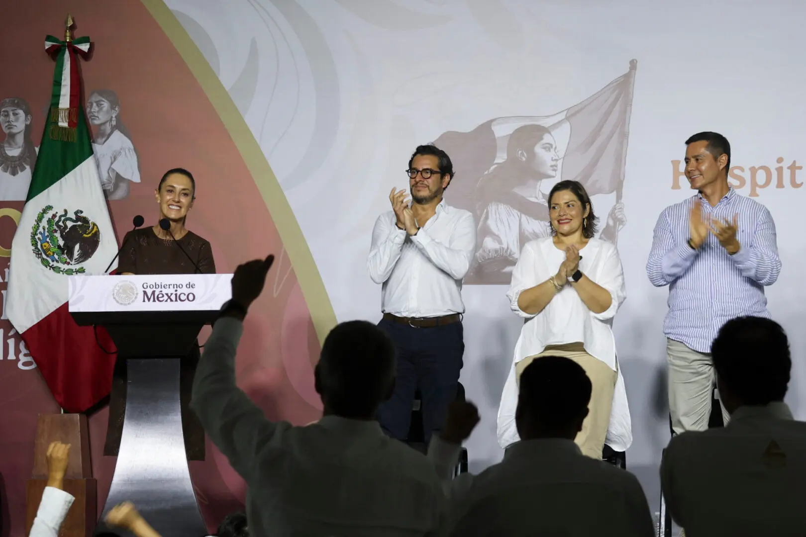 Group applauding on stage beside Mexican flag