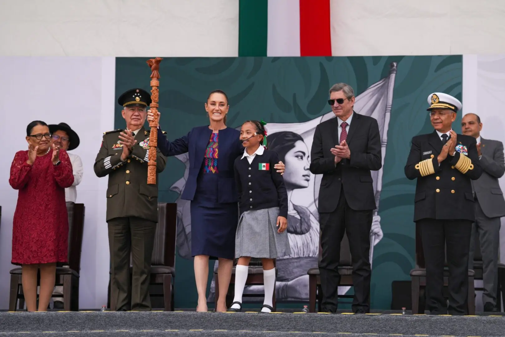 Claudia Sheinbaum celebra con autoridades y una estudiante durante ceremonia conmemorativa en México.