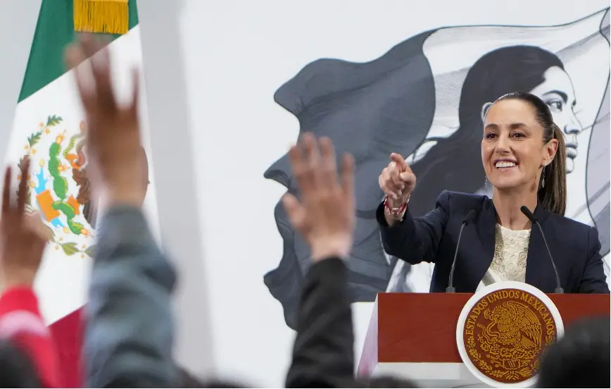 Politician speaking at podium, audience raising hands.