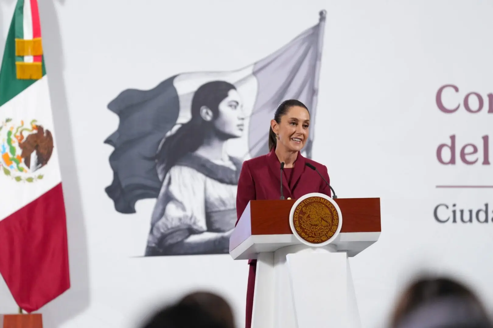 Woman at podium with Mexican flag backdrop