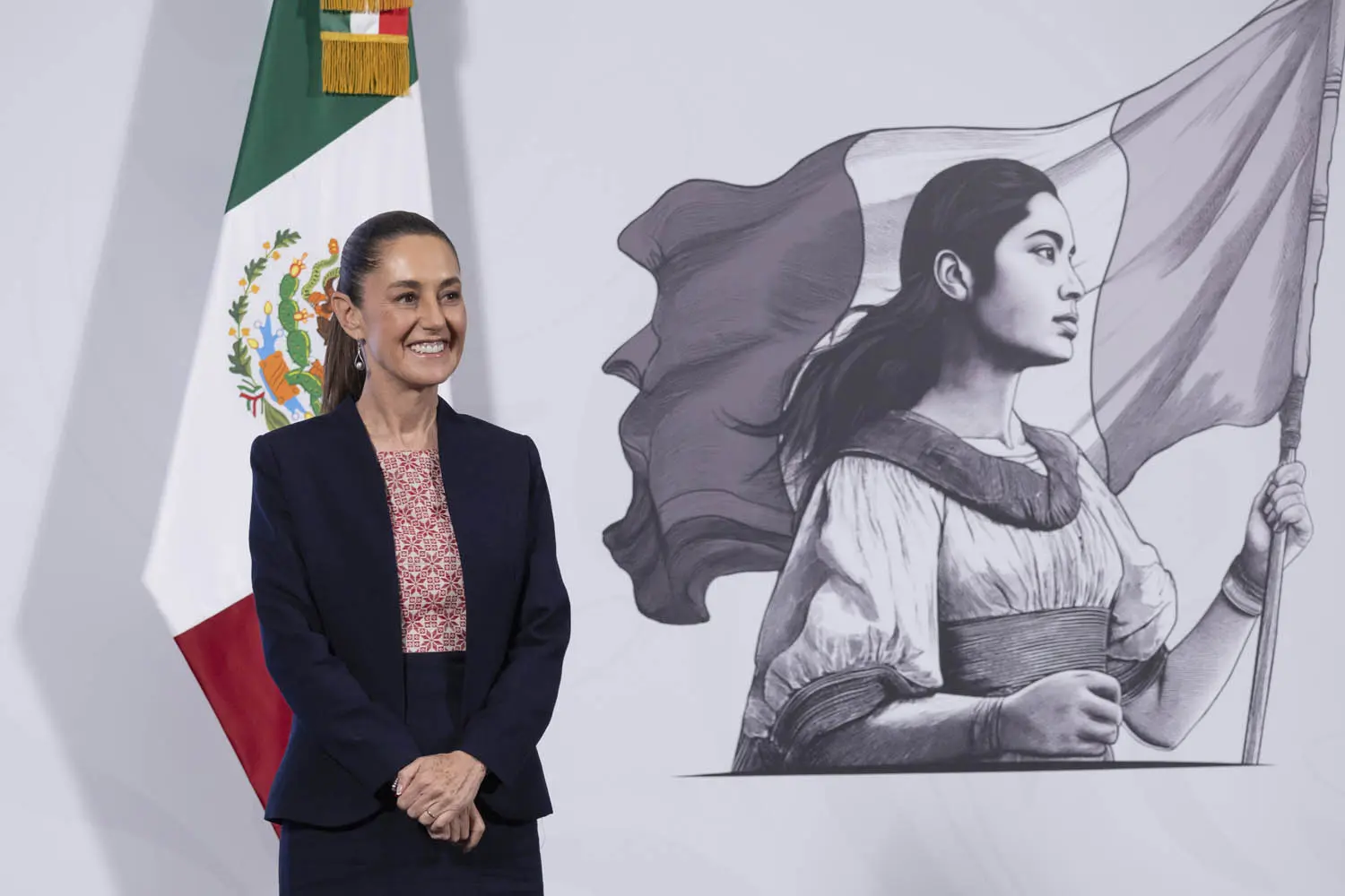 Smiling woman standing beside mural and Mexican flag