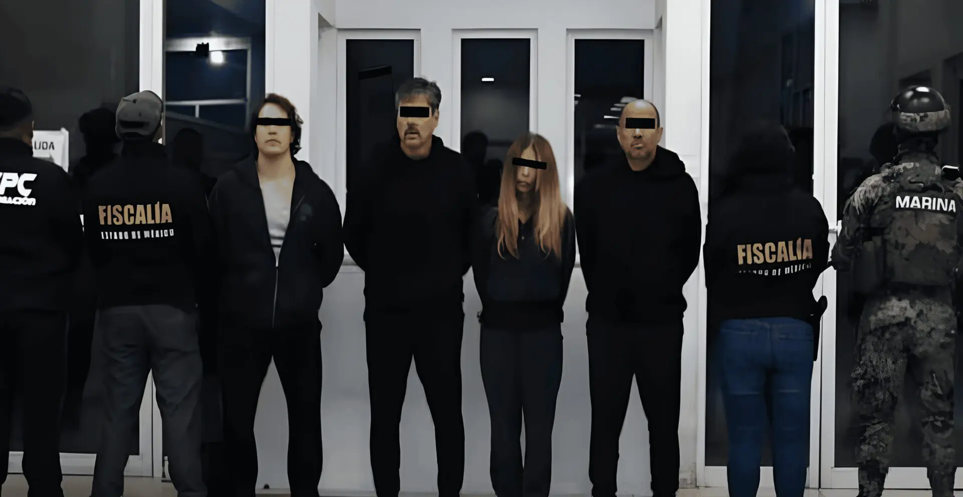 Law enforcement officials and detainees lined against wall