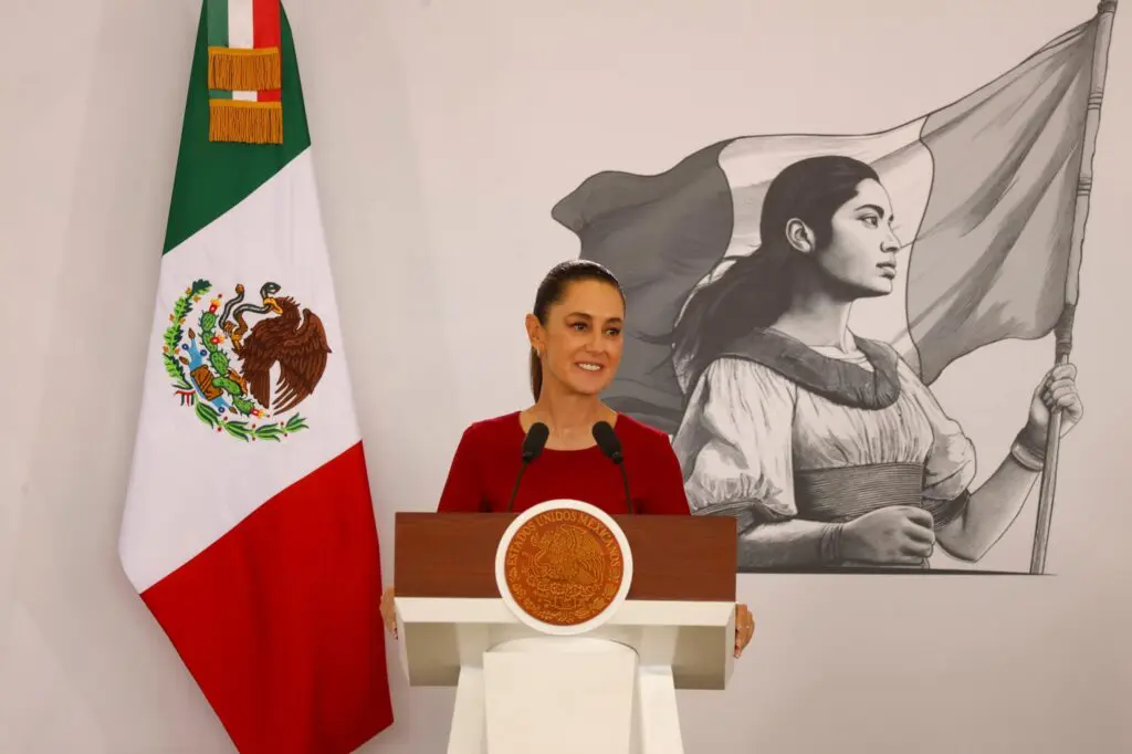 Female speaker beside flag and mural