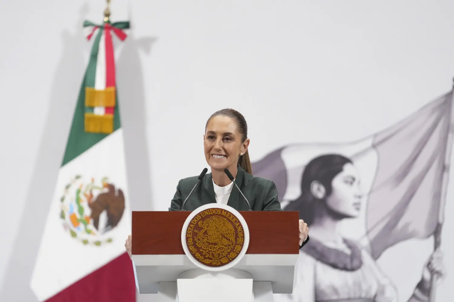 Woman speaking at podium with Mexican flag