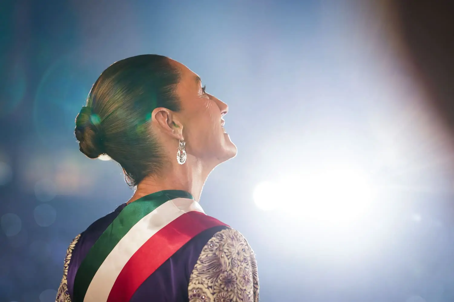 Woman in spotlight with colorful sash.