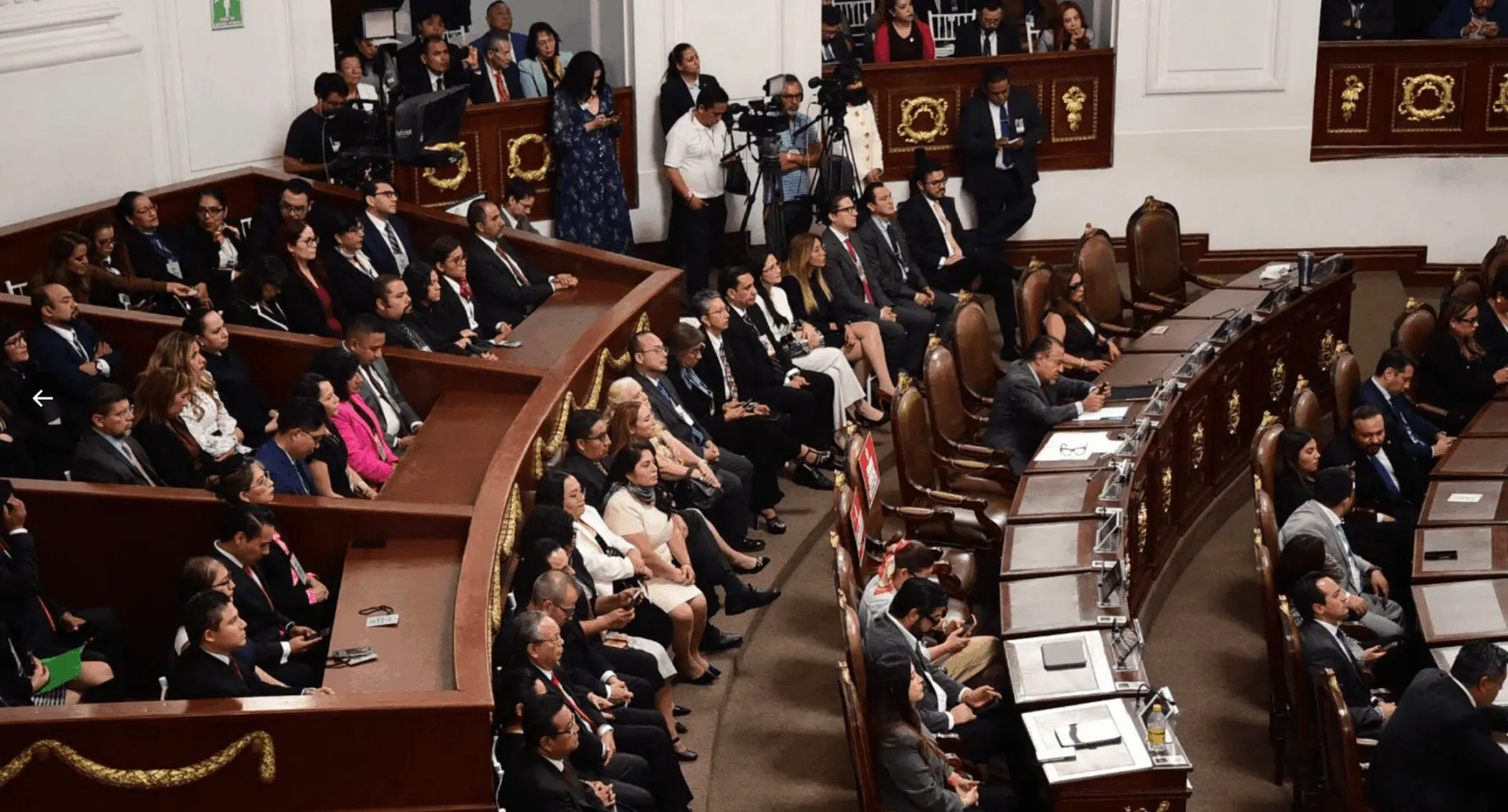 Legislative assembly with seated members and audience.