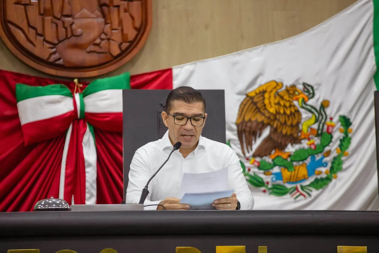 Man reading paper at podium with Mexican flag