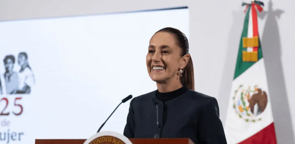 Smiling presenter at podium, Mexican flag in background