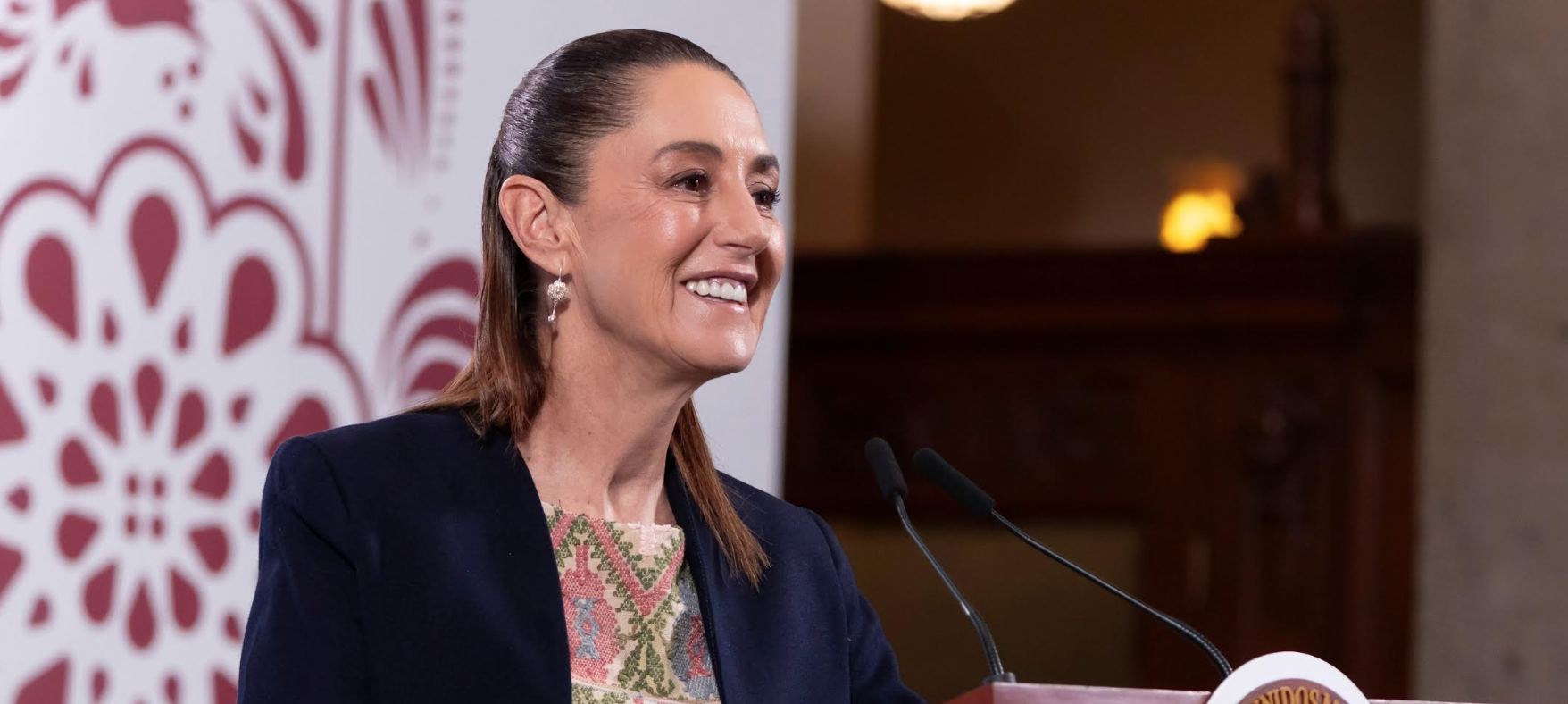 Smiling woman speaking at podium with patterned backdrop