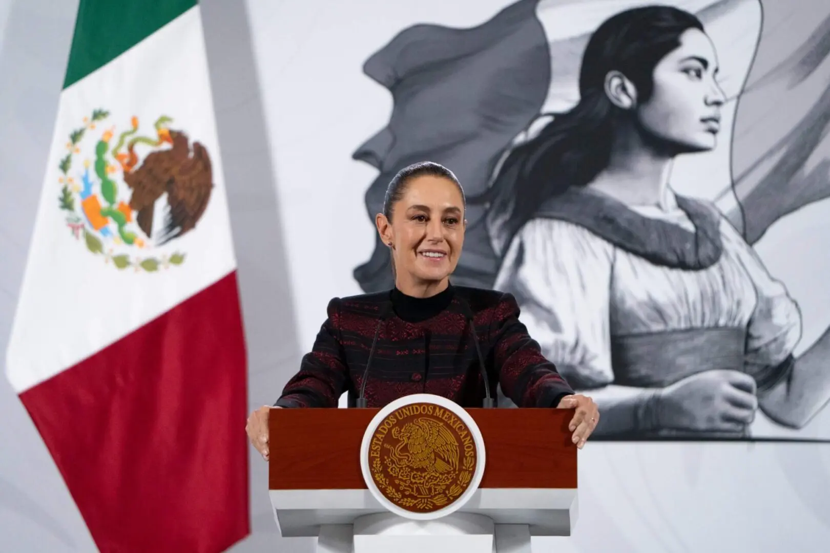 Woman speaking at podium with Mexican flag