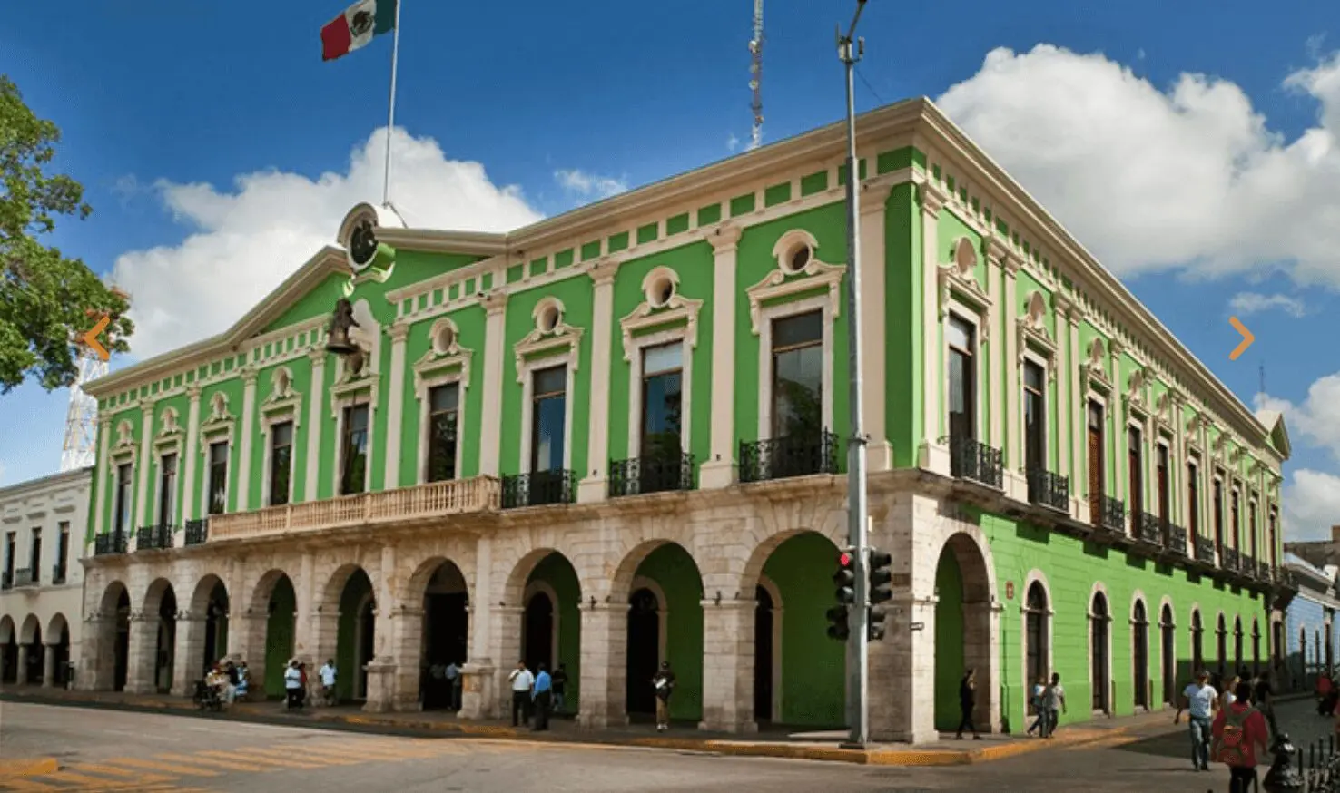 Green historic building with arched windows, flags.