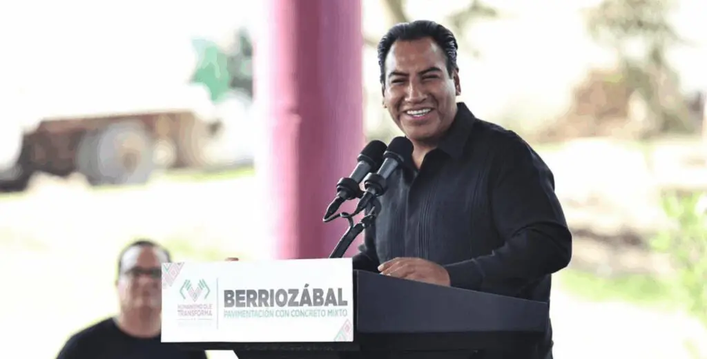 Smiling man speaking at outdoor podium event.