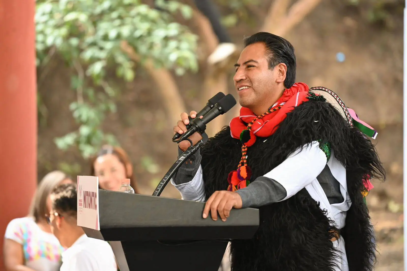 Smiling man in traditional attire speaking at podium