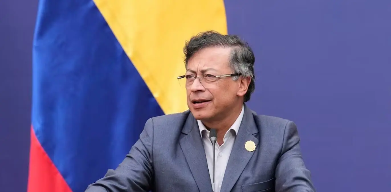 Man in suit speaking at podium with flag