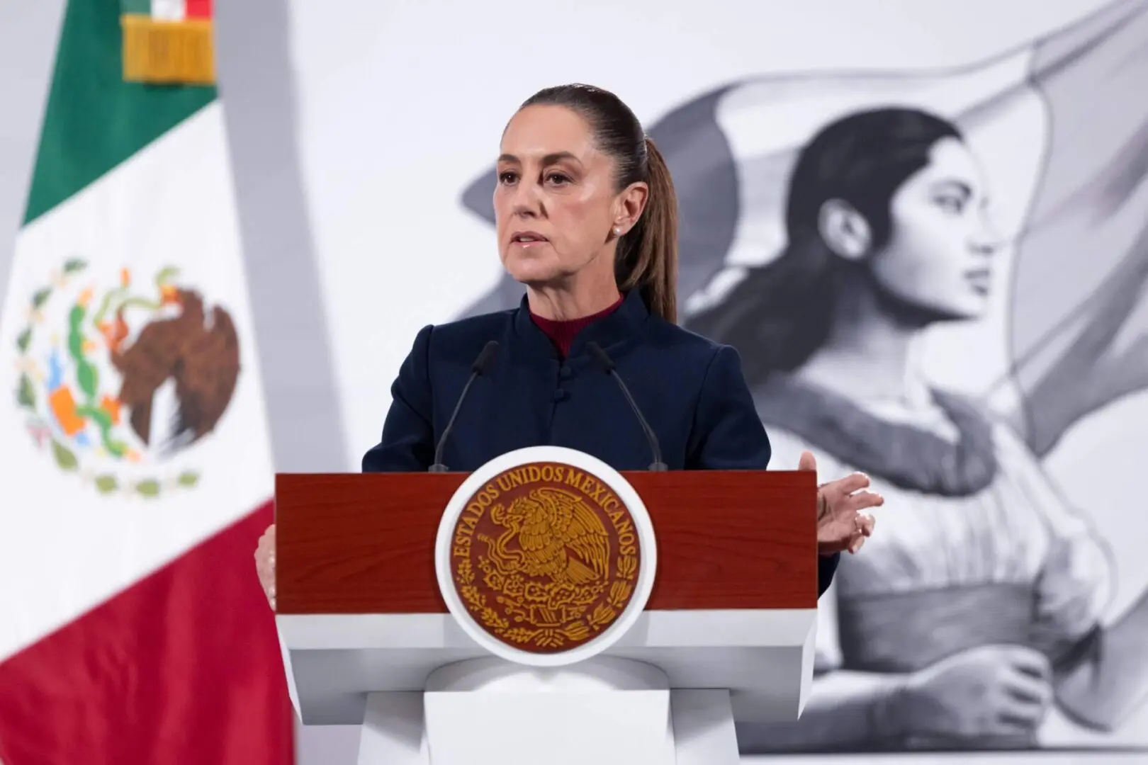 Woman speaking at podium with Mexican flag