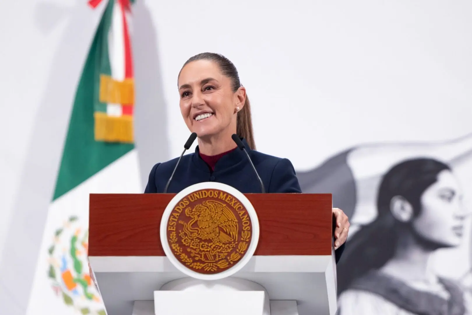 Smiling woman speaking at podium with Mexican flag