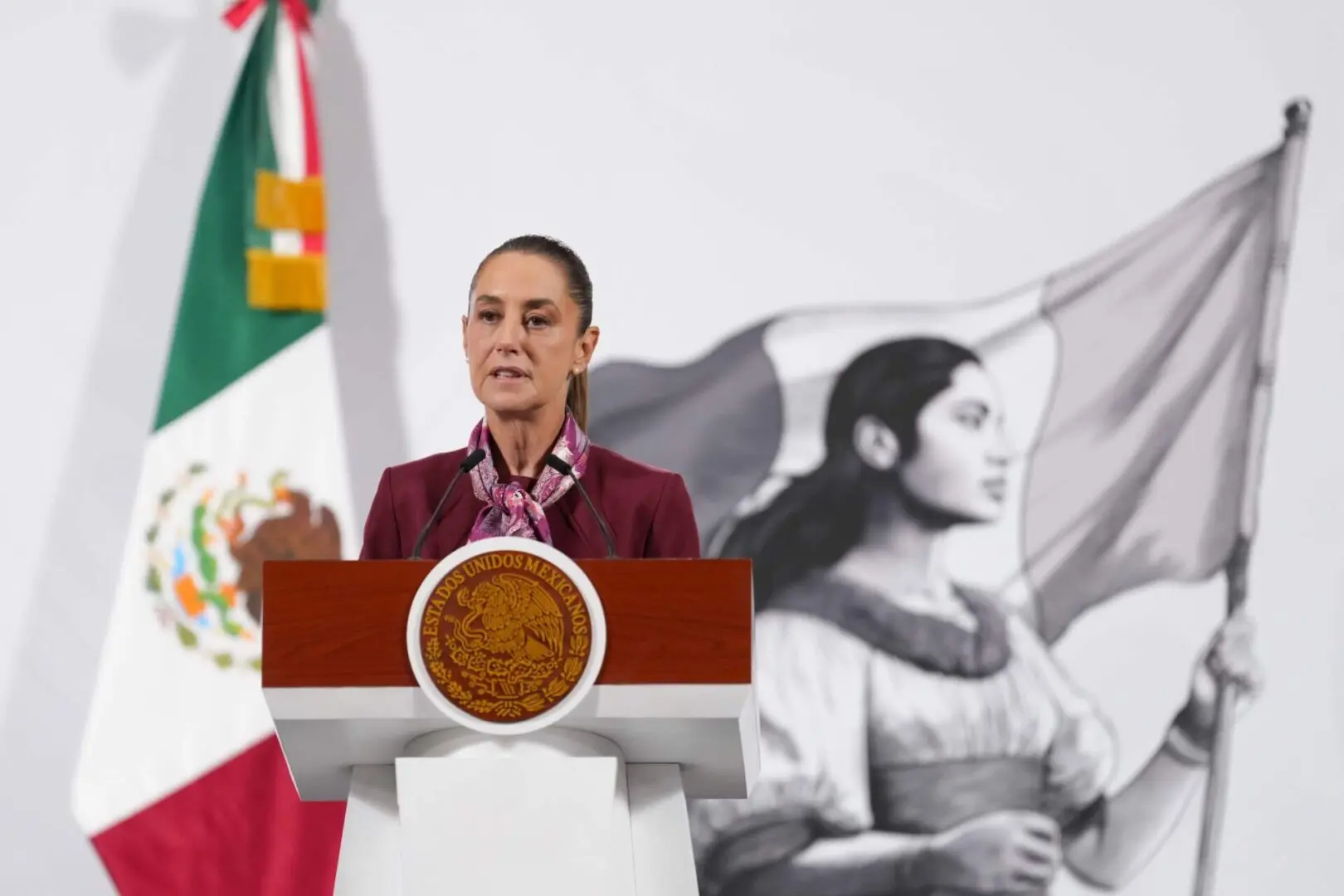 Woman speaking at podium with Mexican flag