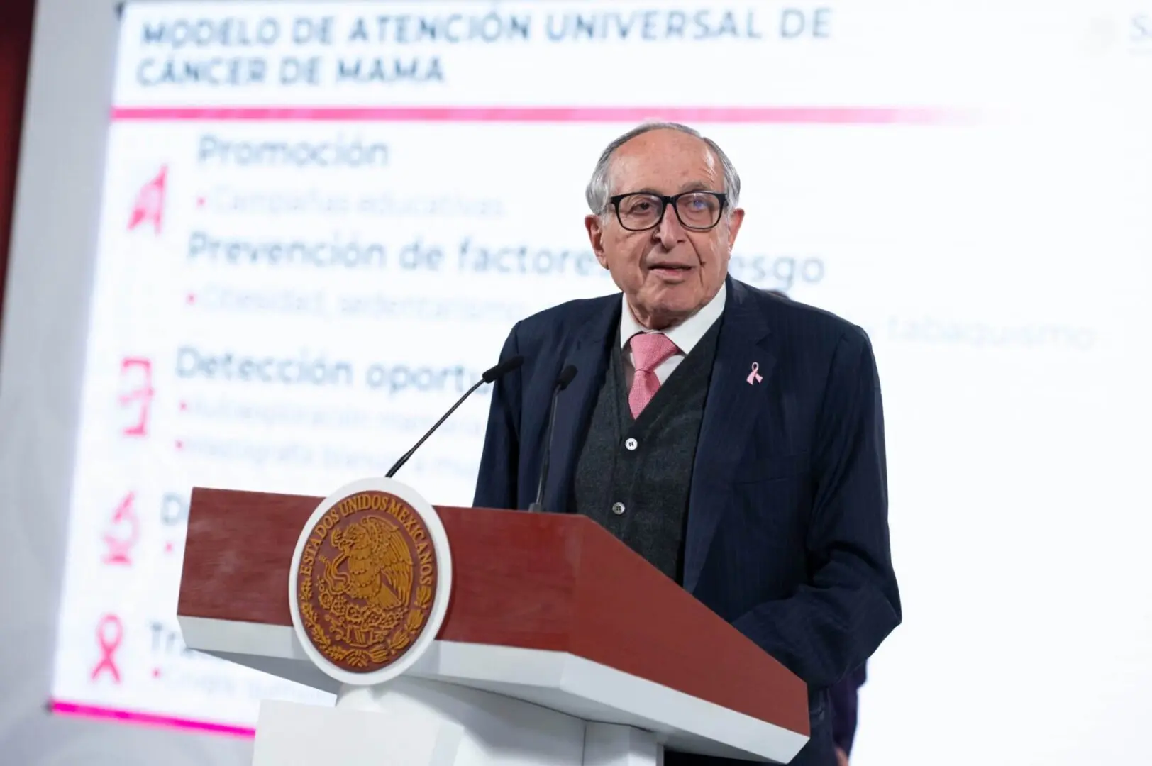 Elderly speaker with pink ribbon at podium