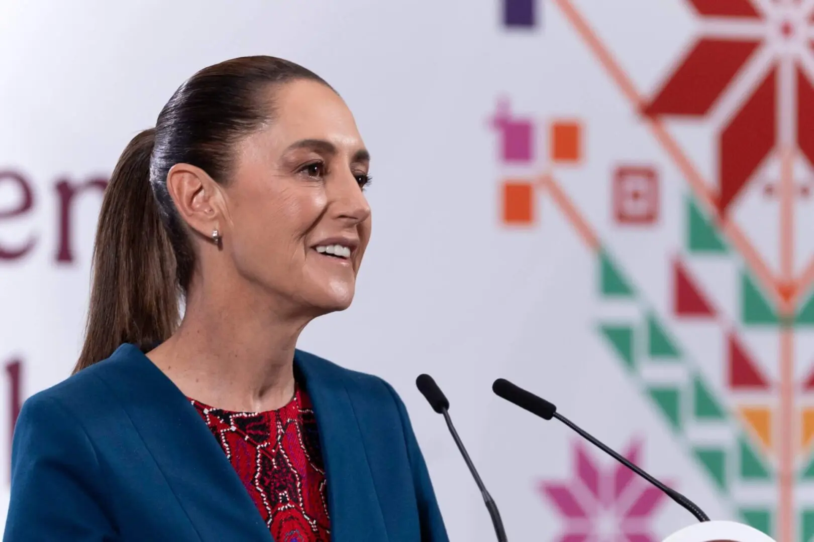 Ponytailed woman speaking at podium, geometric backdrop