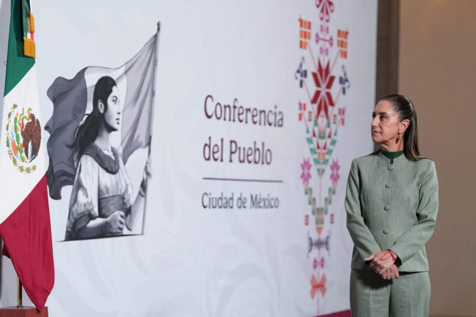 Woman in green suit beside Mexican flag backdrop