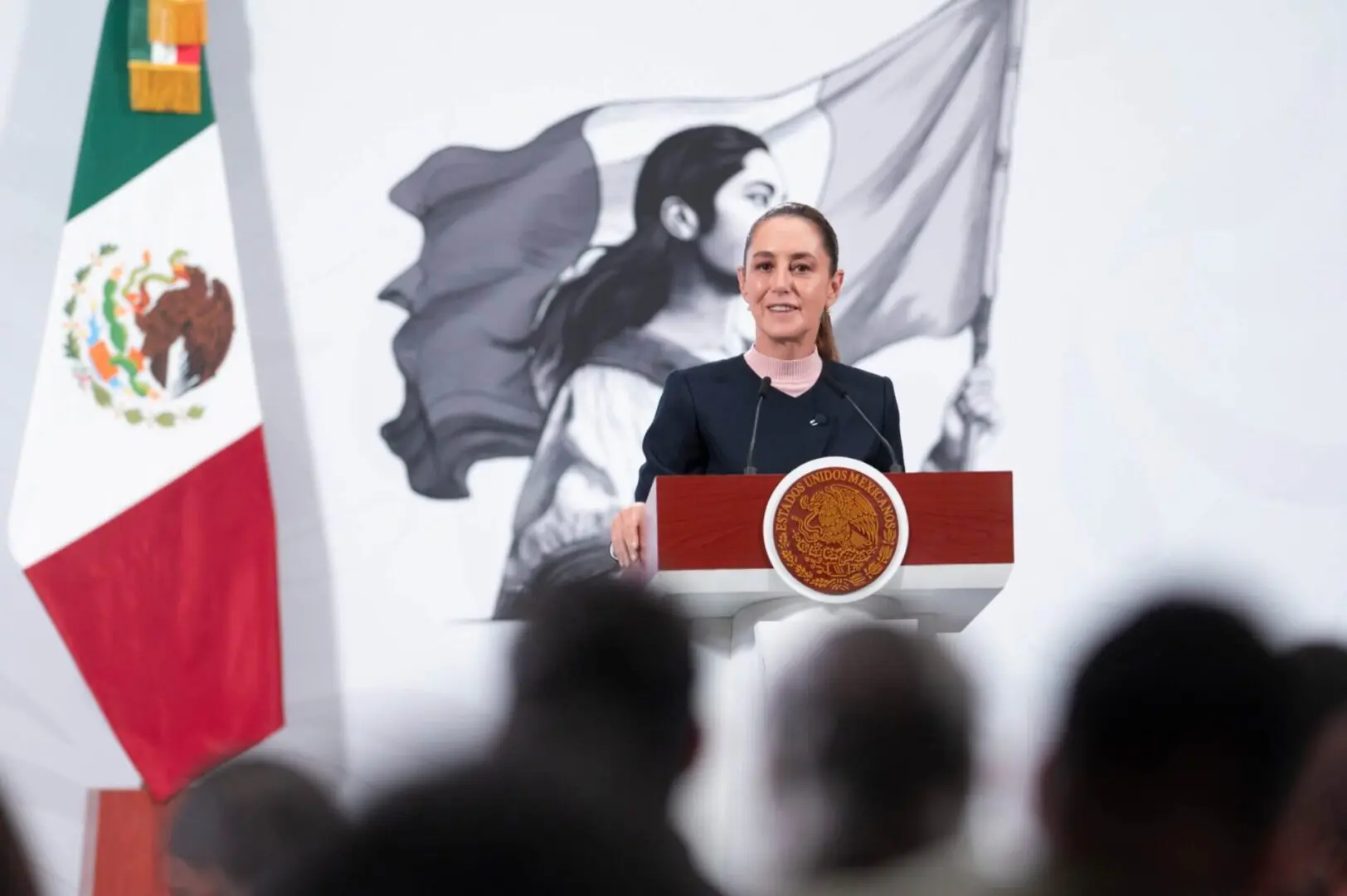 Woman speaking at podium with Mexican flag