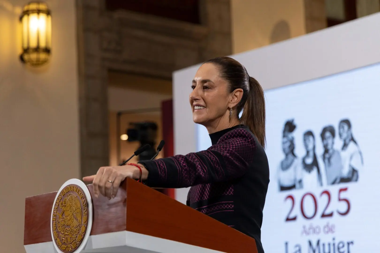 Woman speaking at podium with 2025 banner
