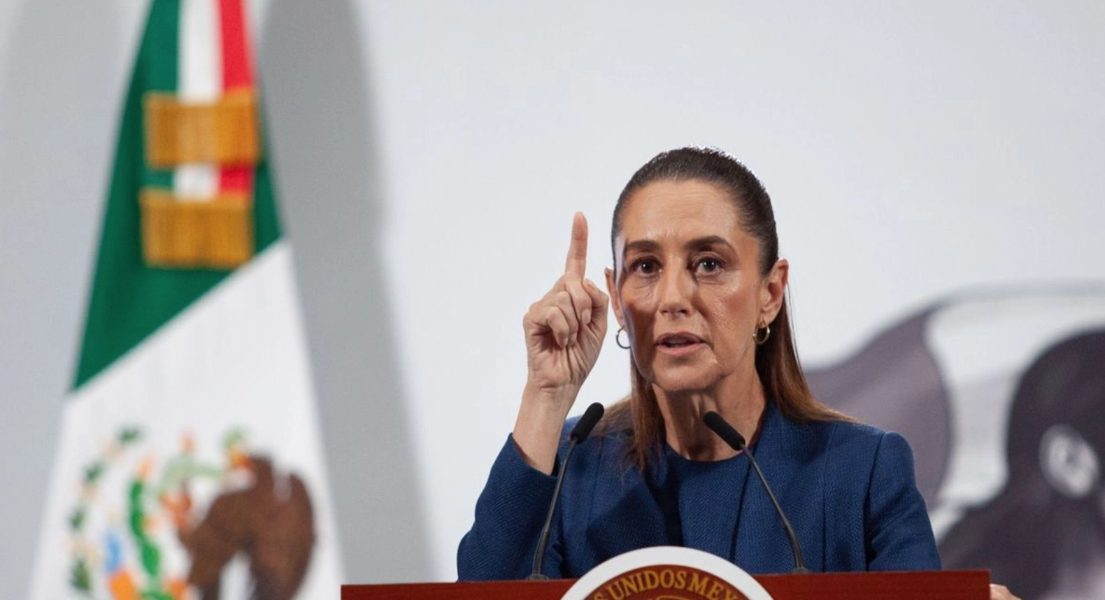 Woman speaking at podium with Mexican flag