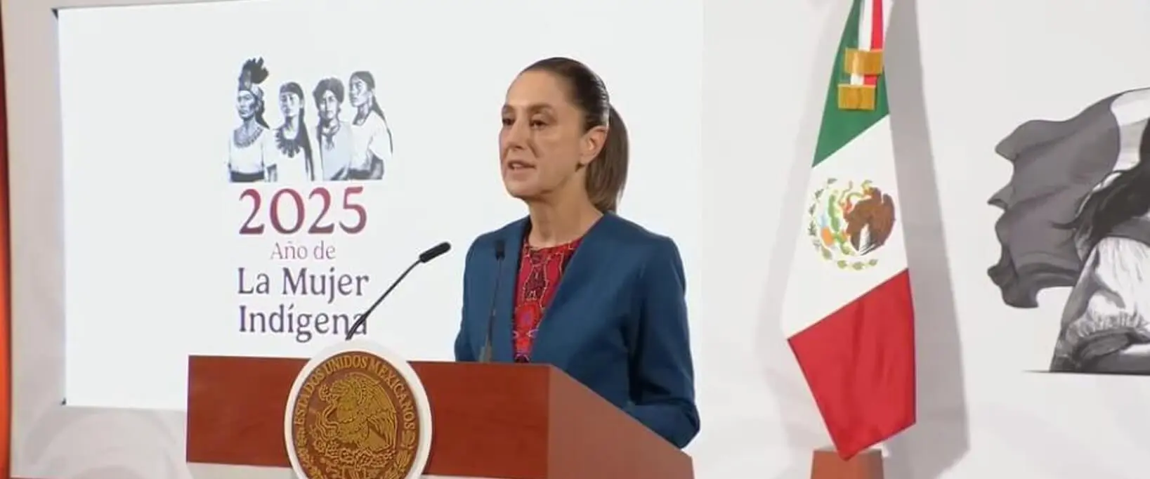 Woman speaking at podium beside Mexican flag