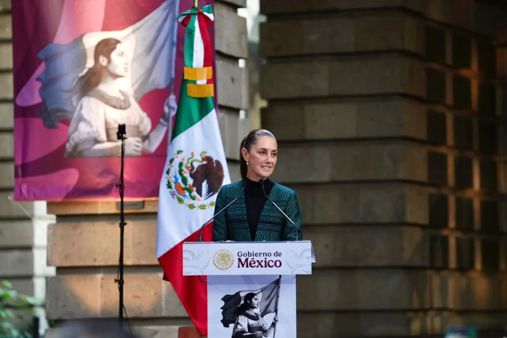 Woman speaking at podium with Mexican flag