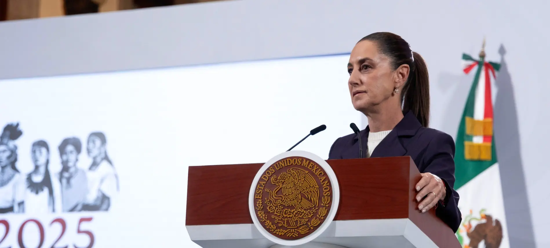 Woman speaking at podium with Mexican flag