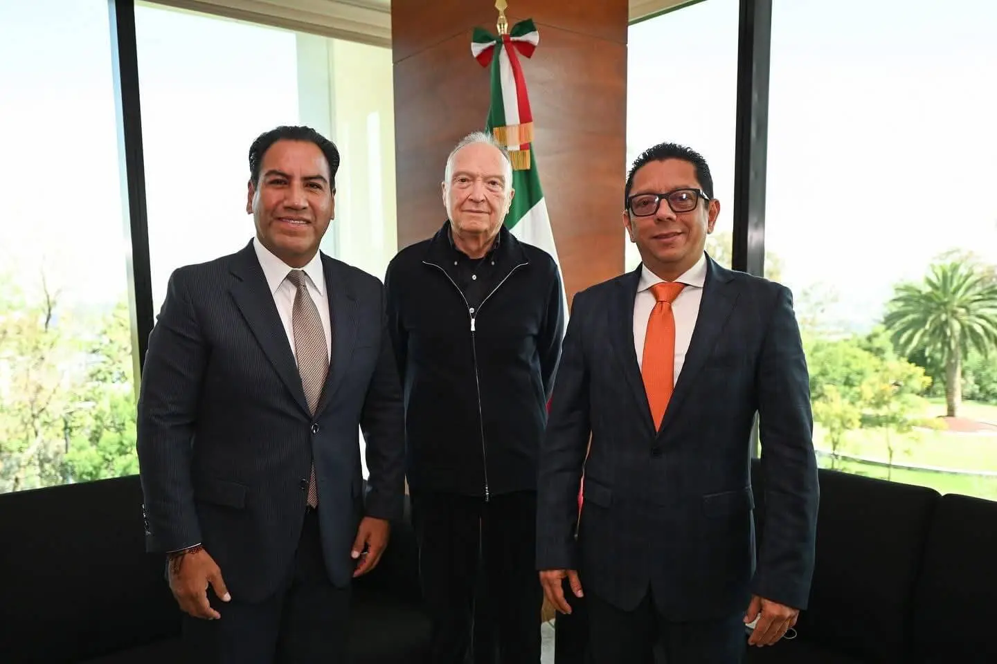 Three men posing in office beside Mexican flag