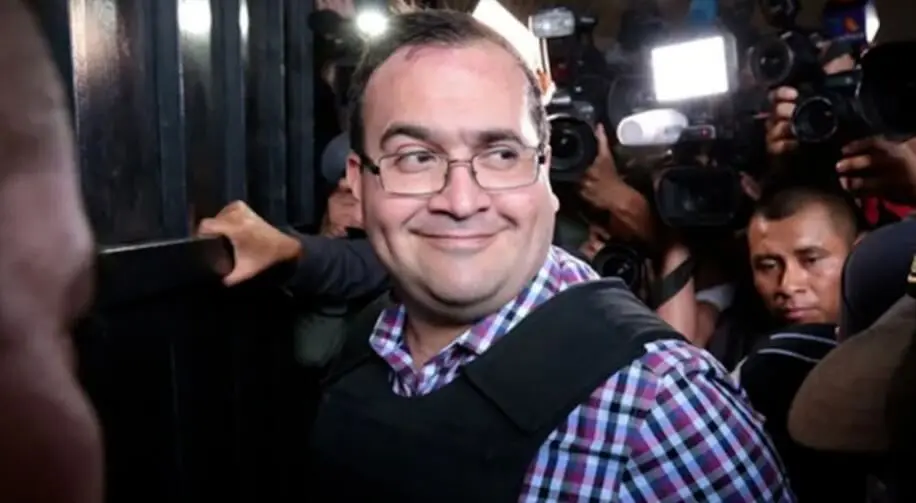 Smiling man escorted through crowded press