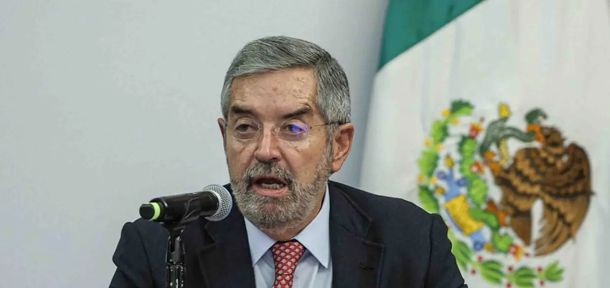 Bearded man speaking at podium, Mexican flag