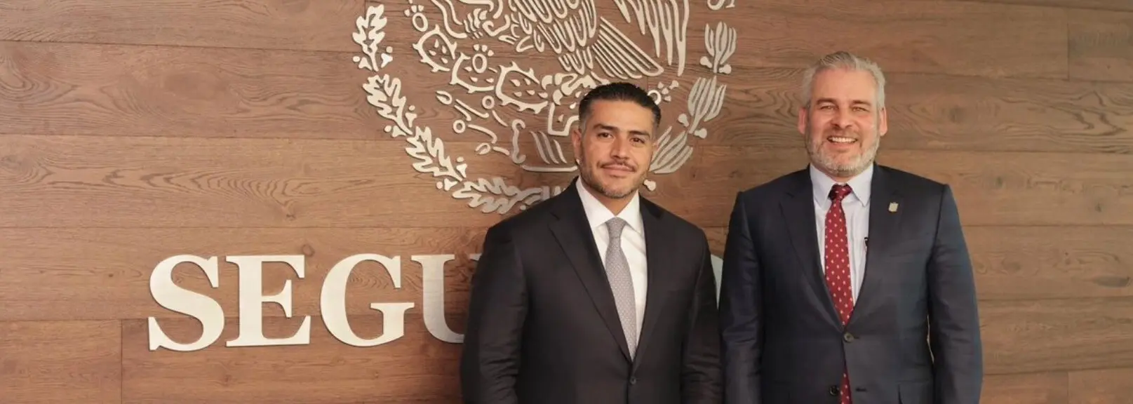 Two men in suits before official seal