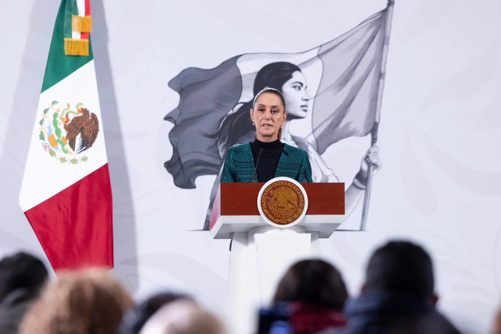 Woman delivering speech at podium with Mexican flag