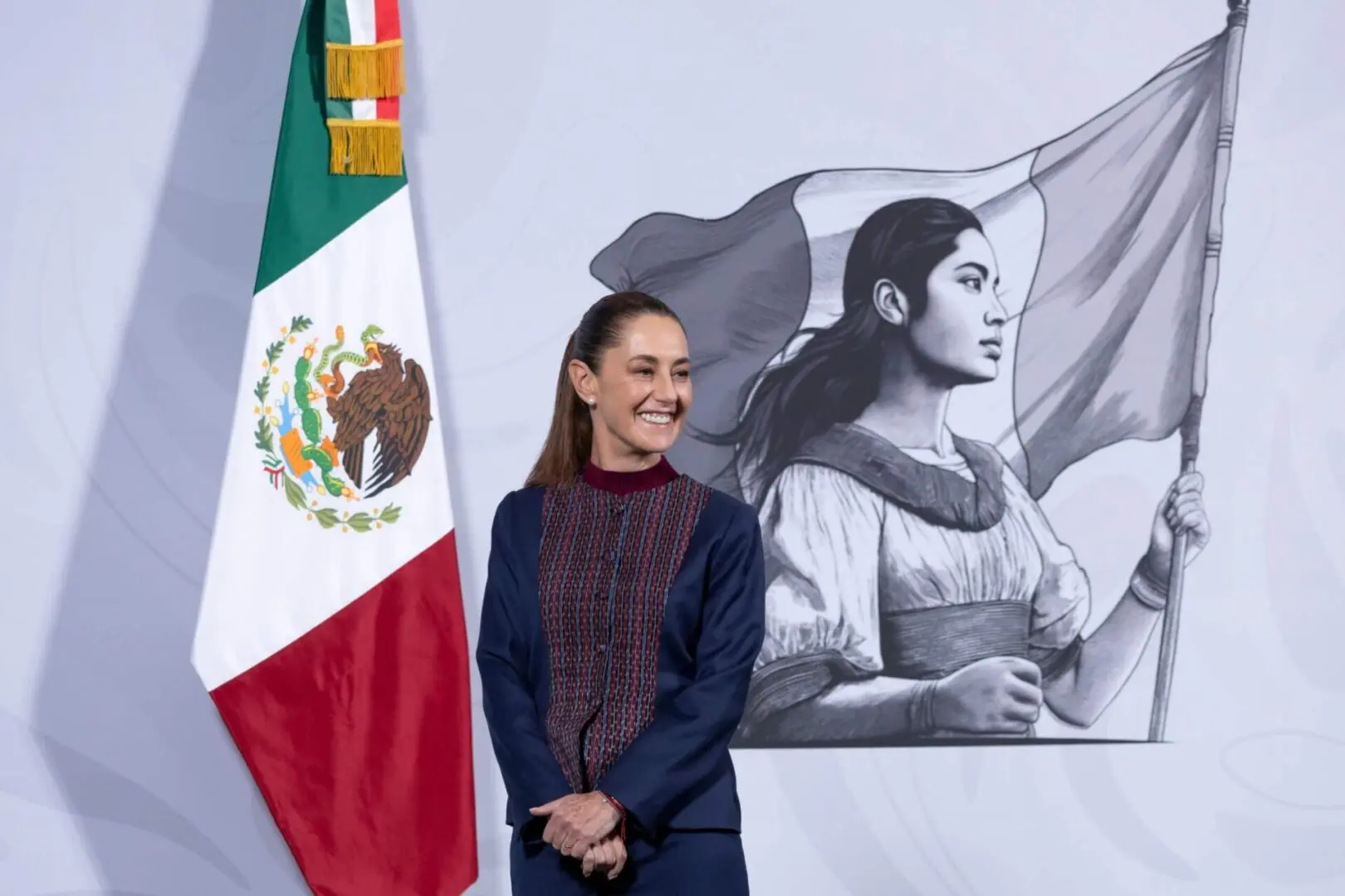 Smiling woman beside Mexican flag and mural